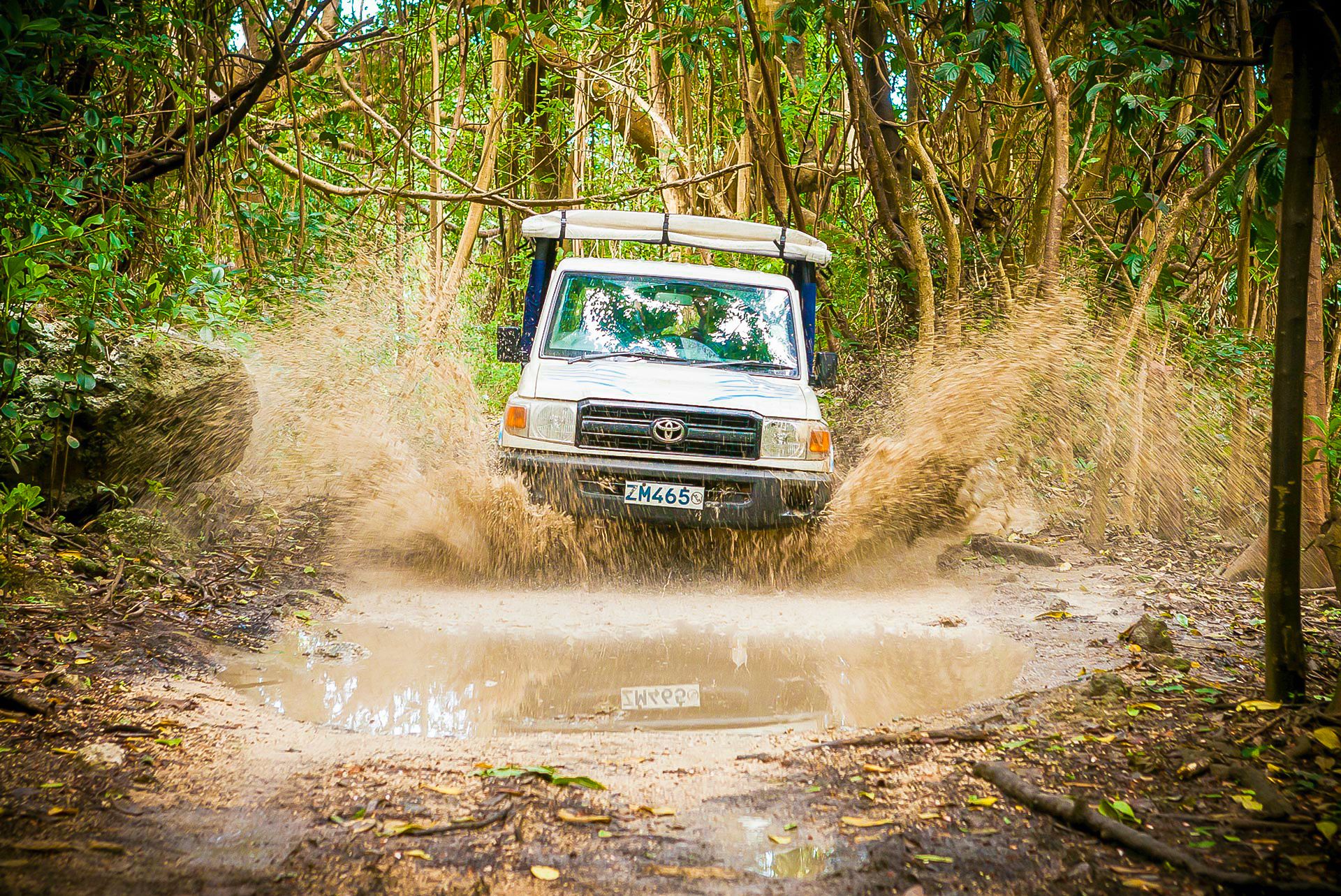safari jeep driving through puddle splashing mud
