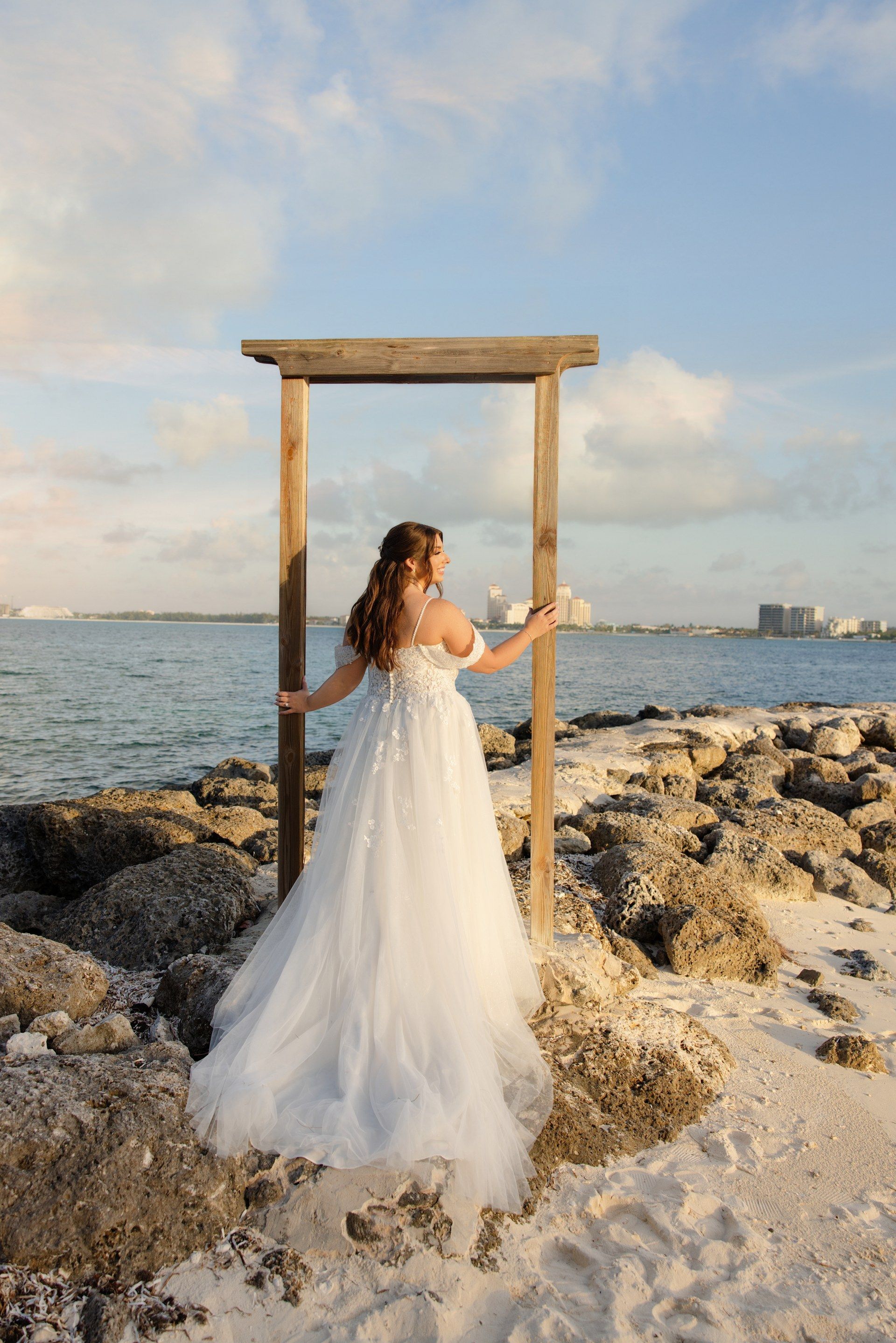 Bride standing in a wooden frame on rocks overlooking the ocean at Sandals Royal Bahamian
