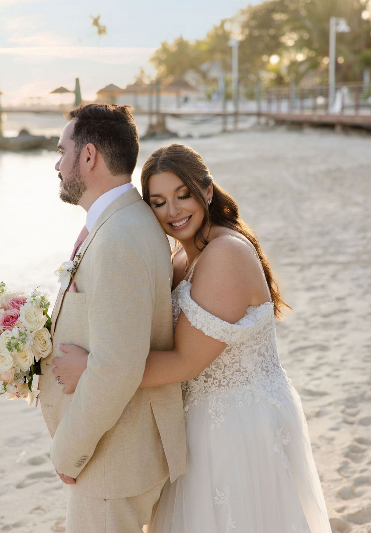 Bride embracing groom with closed eyes on the beach at Sandals Royal Bahamian