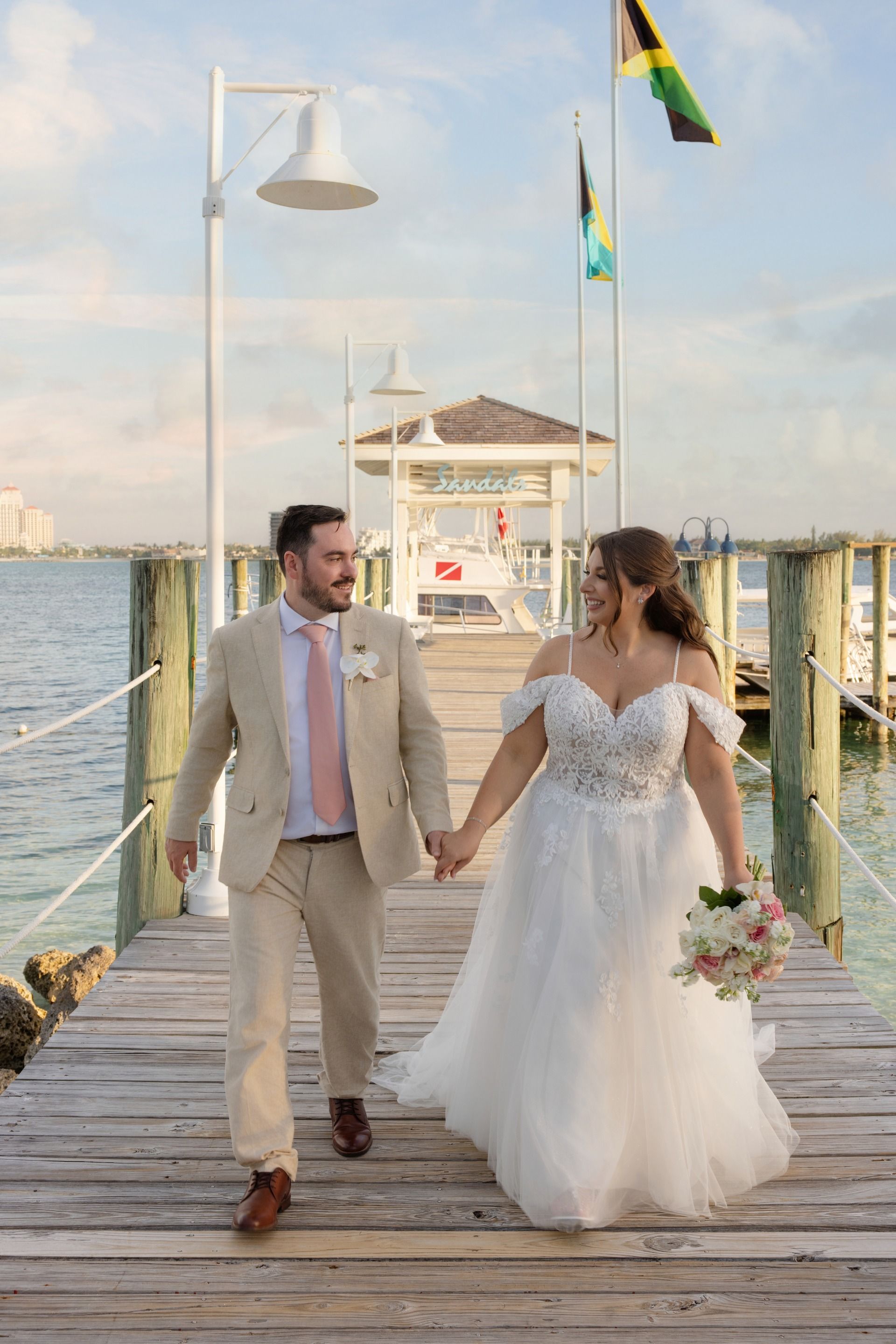 Bride and groom smiling on pier at Sandals with Caribbean flags in the background