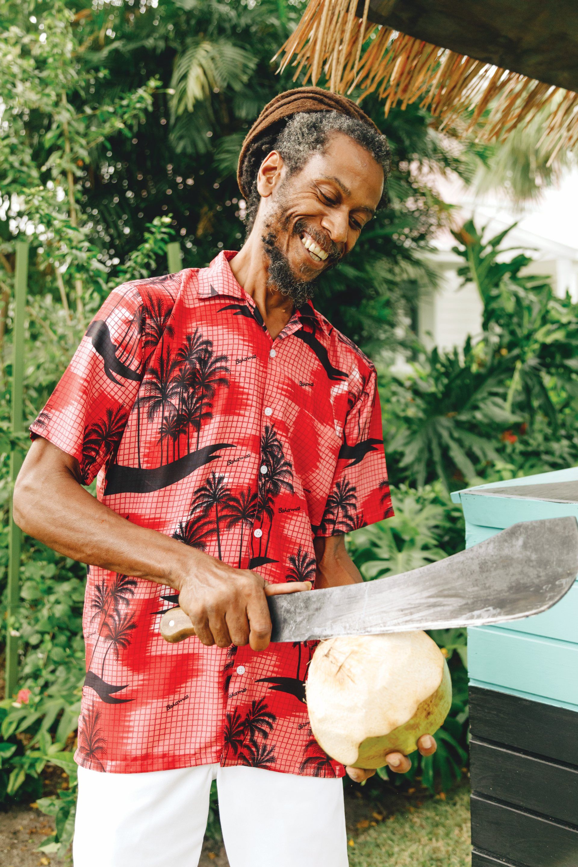 Local vendor cutting a fresh coconut in Nassau Bahamas wearing a traditional Bahamian shirt