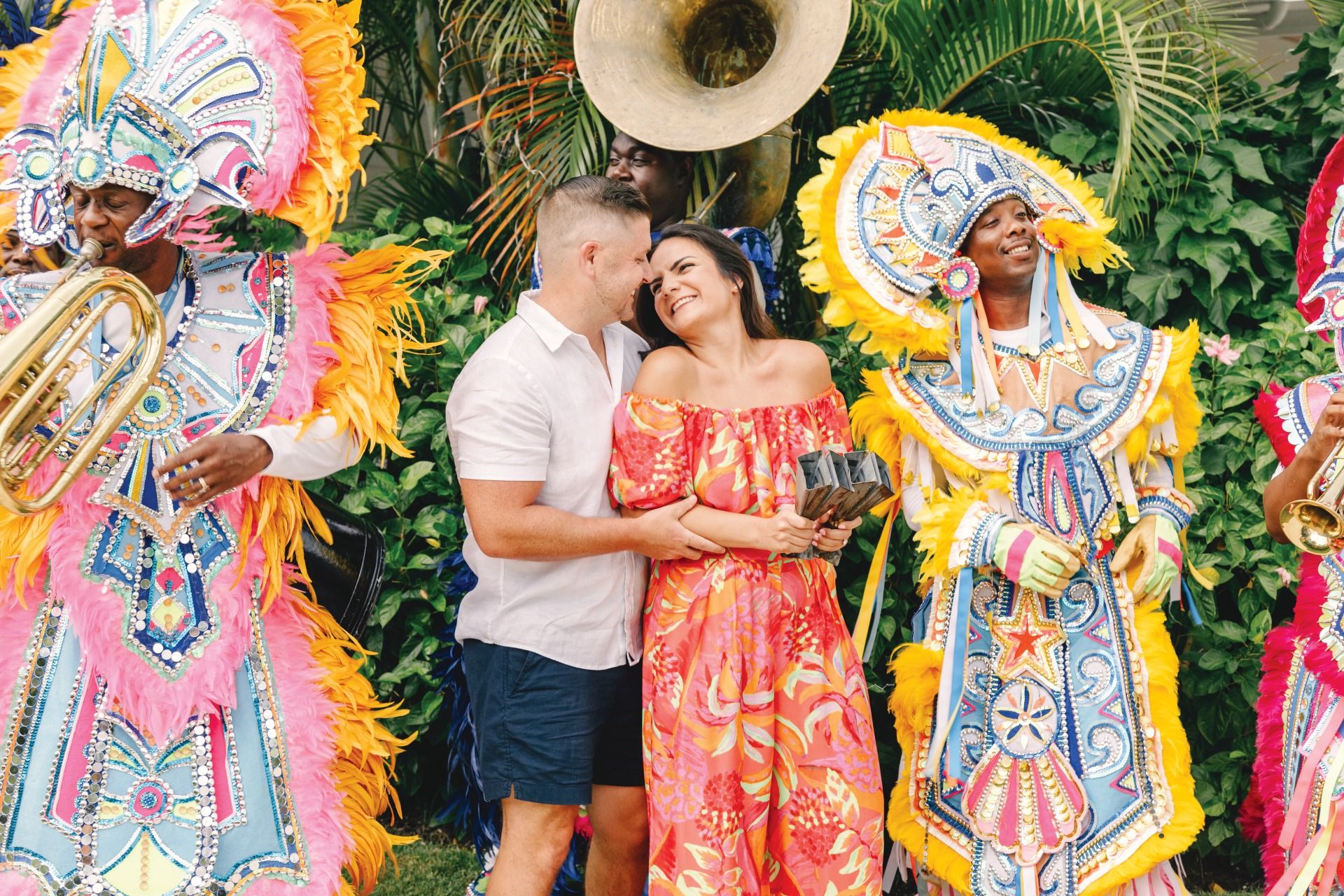 A couple laughs and embraces surrounded by vibrant Junkanoo performers at Sandals Royal Bahamian, Nassau, Bahamas