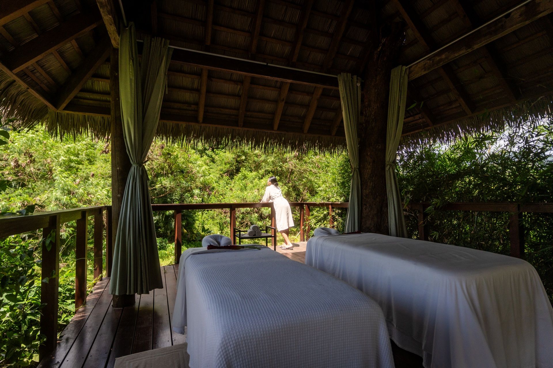 Two outdoor massage tables in an open-air treehouse pavilion surrounded by lush tropical rainforest at the Red Lane Spa, Sandals Saint Vincent